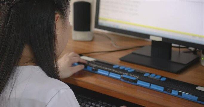 Rear view of woman with blindness disability using computer keyboard and braille display or braille terminal a technology assistive device for person with visual disabilities, handheld shot.