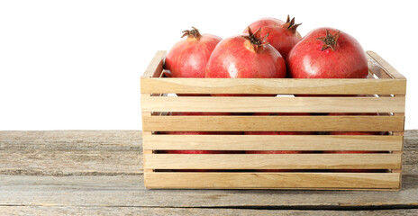 Fresh pomegranates in crate on wooden table against white background