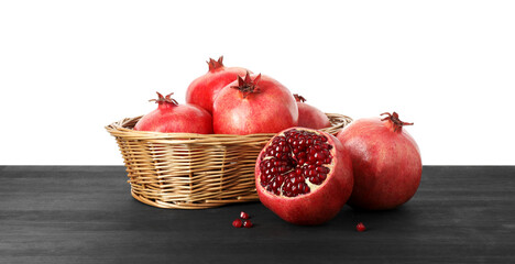 Fresh pomegranates in wicker basket on black wooden table against white background