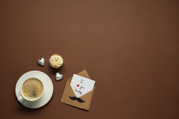 Father's day celebration. Card with phrase I Love You Daddy, cup of aromatic coffee, cupcake and heart shaped candies on brown background, flat lay. Space for text - Powered by Adobe