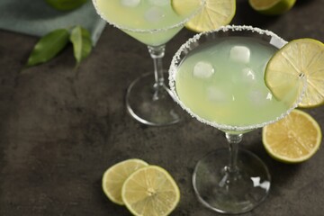 Delicious Margarita cocktail with ice cubes in glasses and lime on grey table, space for text