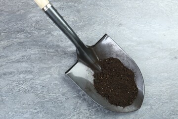 Metal shovel with fertile soil on gray textured surface, above view