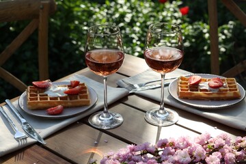 Delicious Belgian waffles with fresh strawberries and wine served on table in spring garden