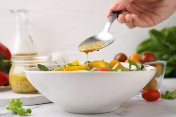 Woman pouring tasty vinegar based sauce (Vinaigrette) from spoon into bowl with salad at white...
