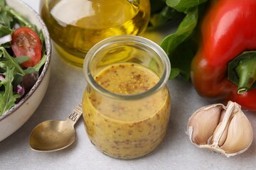 Tasty vinegar based sauce (Vinaigrette) in jar, salad and products on light table, closeup