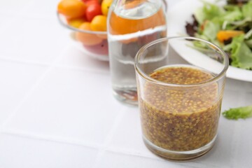 Tasty vinegar based sauce (Vinaigrette) in glass on light tiled table, closeup. Space for text