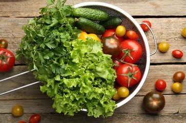 Fresh vegetables in colander on wooden table, flat lay