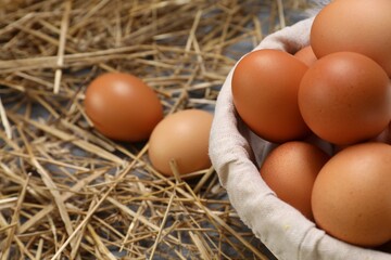 Fresh chicken eggs in bowl and dried straw on table, closeup. Space for text
