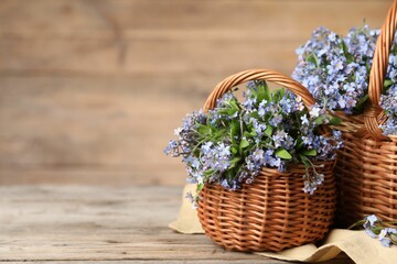 Beautiful forget-me-not flowers in wicker baskets on wooden table, closeup. Space for text