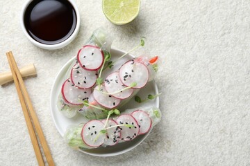 Delicious spring rolls, chopsticks, soy sauce and lime on light grey table, flat lay. Space for text