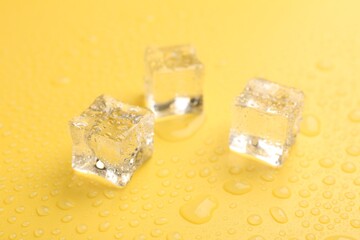 Crystal clear ice cubes on yellow background, closeup