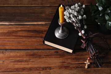 Rosary beads, Bible, burning candle and willow branches on wooden table, above view. Space for text