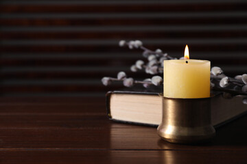 Burning candle, Bible and willow branches on wooden table, closeup. Space for text