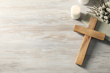 Burning candles, cross, book and willow branches on wooden table, flat lay. Space for text