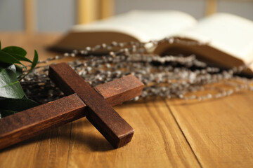 Cross and willow branches on wooden table, closeup