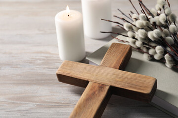 Burning candles, cross, book and willow branches on wooden table, closeup