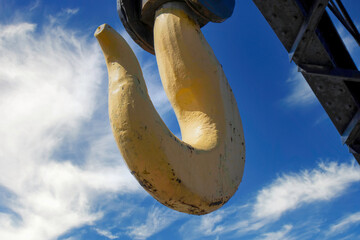 Large yellow metal hook hanging from a railway crane car, blue sky clouds in background, nobody