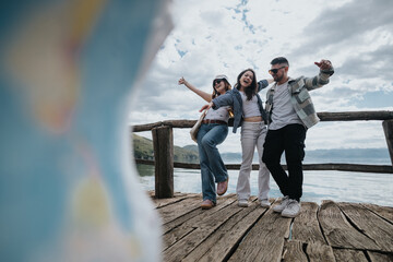 Three happy tourists share a laughter-filled moment on a rustic wooden pier by a picturesque lake,...