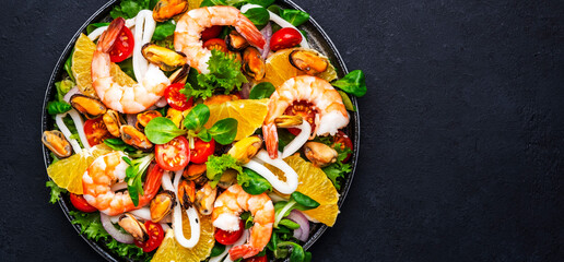 Delicious salad with shrimp, mussels, squid, oranges, lamb lettuce and olive oil with lemon juice dressing, black table background, top view banner