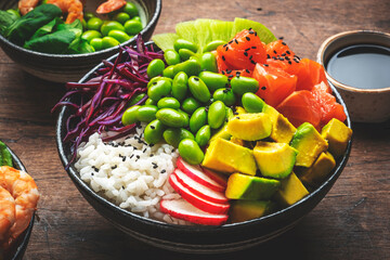 Balanced diet poke bowls with tuna, salmon, shrimp, vegetables, legumes, avocado and rice, wood table background, top view