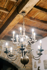 Bronze glowing chandelier with spheres and candle lamps hangs from a wooden ceiling