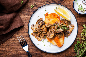 French breaded chicken steak with mushrooms and onion sauce with white wine, lemon and thyme on plate, rustic table background, top view