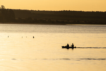 Obraz na płótnie Canvas paisaje relajante con siluetas de canoas de pescadores en la hora dorada dejando una estela en el río, Entre Ríos, Argentina 