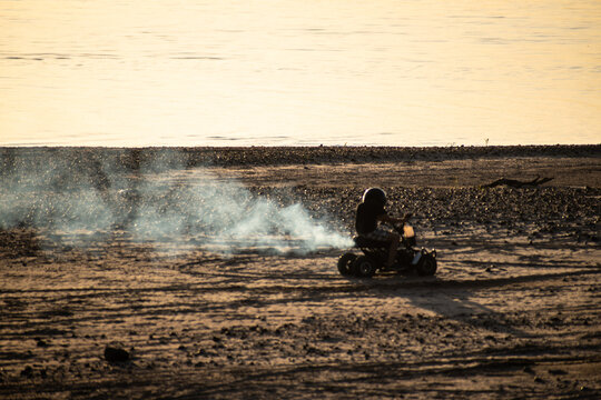 Ni&ntilde;o manejando un cuatriciclo sobre el arena de la playa y su humo al atardecer. Argentina