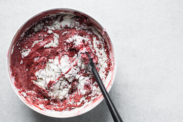 Top view of flour being folded into Red velvet cake batter in white ceramic mixing bowl, process of...