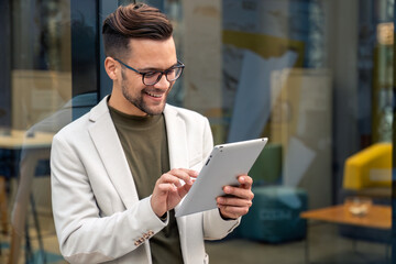 Young business man manager wearing suit using digital tablet for work outside modern Cafe.