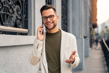 Good looking businessman talking on the phone while walking down the city street.