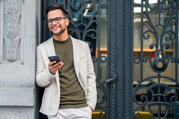 Smiling successful male business person using smart phone while standing outside a modern business...