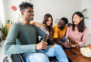 Group of diverse millennial teenage people having fun together at home. Inclusion and diversity concept with young indian man in wheelchair hanging out bonding with friends at apartment.