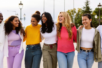 Young multicultural group of women walking together at city street. Empowerment concept with united diverse girls from different countries embracing each other while bonding outdoors.