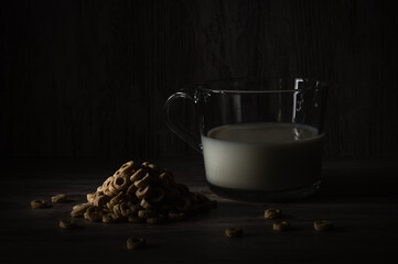 a pile of cereals next to a translucid glass with some milk, in a dark food style photopraphy
