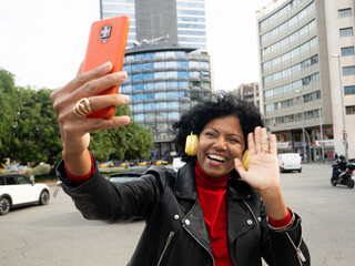 African American middle aged woman influencer making a video with smartphone in a city