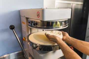 closeup shot of chef's hands holding dough to put it in the machine and prepare pizza. High quality photo - Powered by Adobe