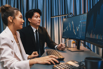 Smiling Asian business traders pointing to dynamic stock exchange data screen profit value online...
