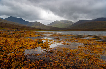 Dramatic view of Scottish loch lake and mountains with golden evening light and dark clouds in sky. Breathtaking landscapes show the power of nature