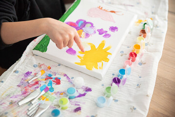 Cute little child painting with paintbrush and colorful paints. Kid hands start painting at the...