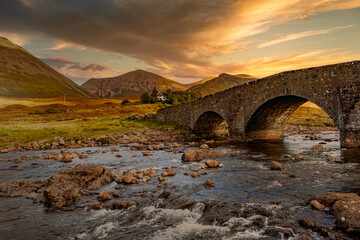 Sligachan Bridge, Isle of Skye, Scotland, with Cuillin Mountains and orange clouds on backround in...