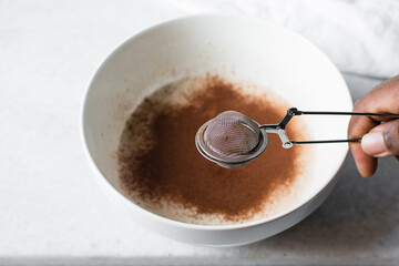 a silver strainer with Cocoa powder, sieving clumpy cocoa powder into batter