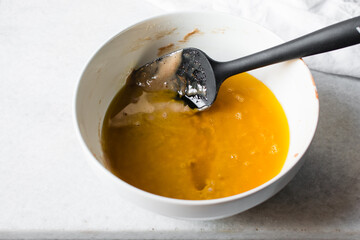 Mixing Melted butter and Madeleine batter in a white mixing bowl