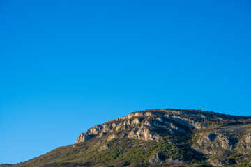 Landscape photos of nature. A tower on top of a mountain. Clear blue sky above the mountain.
