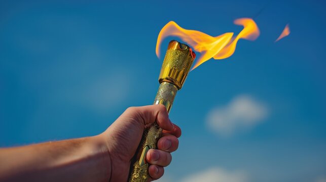 A man's hand holds a torch with the olympic flame against a blue sky background. Sport concept