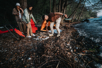 Young adults gather wood for a campfire by a lake, highlighting a serene outdoor camping experience...