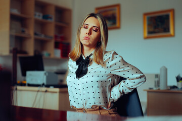 Tired Businesswoman Having Back Pains at her Desk. Corporate worker suffering from side effect of a...