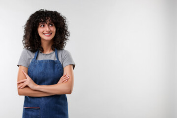 Happy woman wearing kitchen apron on light grey background, space for text. Mockup for design