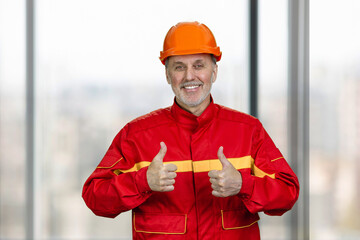 Portrait of a smiling handyman construction worker showing both thumb up. Blurred windows background.