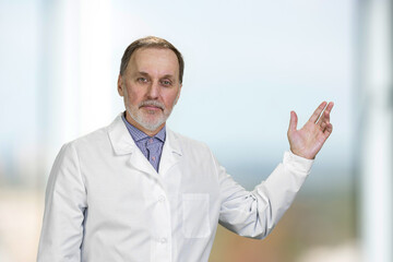 Portrait of senior doctor pointing up showing on copy space. Indoor blurred background.